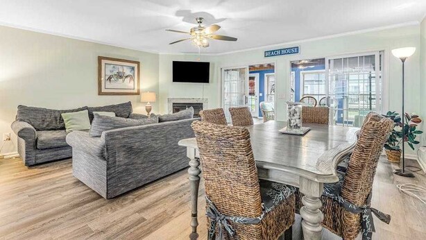 A living room with a sofa, a dining table with chairs, a ceiling fan, and a sign reading 'BEACH HOUSE'. - Versailles at Eagles Landing townhome with pool & tennis - walk to beach shuttle (Rehoboth Beach)