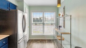 A kitchen with a stainless steel refrigerator, a window with blinds, a metal shelf unit, and a pendant light. - Versailles at Eagles Landing townhome with pool & tennis - walk to beach shuttle (Rehoboth Beach)