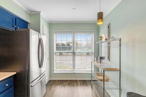 Una cocina con un refrigerador de acero inoxidable, una ventana con persianas, un estante metálico y una lámpara colgante.