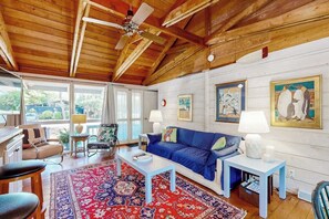A spacious living room with a blue sofa, a red patterned rug, and wooden ceiling beams. - Dewey Beach cottage 1 block from the beach, dog friendly (Dewey Beach)