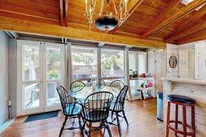 A dining area with a round table and chairs, a chandelier, and a view through large glass doors. - Dewey Beach cottage 1 block from the beach, dog friendly (Dewey Beach)