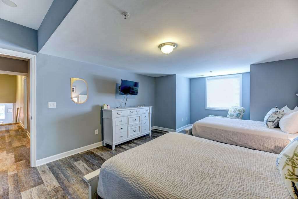 Un dormitorio con dos camas, un aparador, un televisor y una ventana.