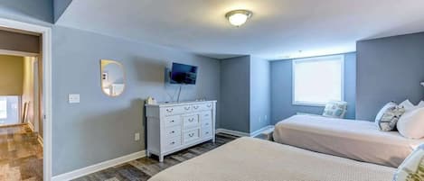Un dormitorio con dos camas, un aparador, un televisor y una ventana.