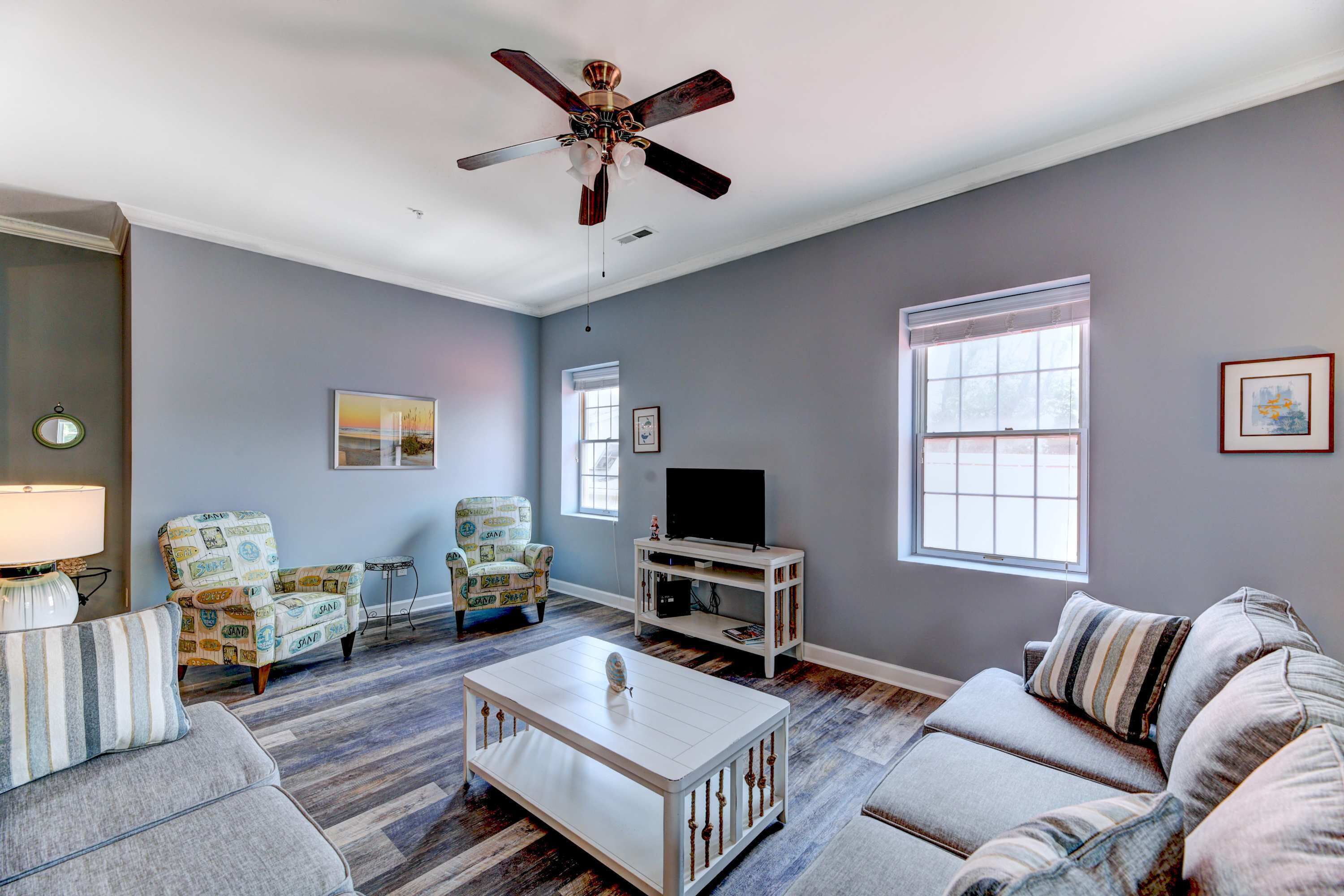 A living room with a ceiling fan, a television on a stand, and two sofas.