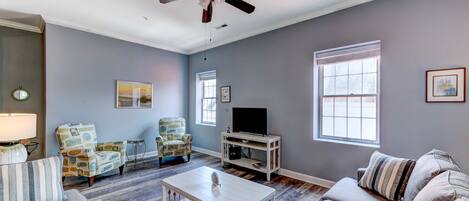 A living room with a ceiling fan, a television on a stand, and two sofas.