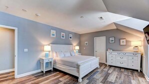 Quarto com cama, mesas de cabeceira, cômoda e porta.