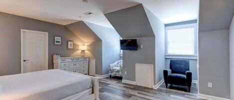 Ein Schlafzimmer mit Bett, Kommode, Stuhl und einem an der Wand befestigten Fernseher.