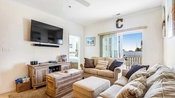A living room with a flat-screen TV, a wooden cabinet, a beige sofa, and a large window with blinds. - Sandpiper Villages condo with fast WiFi, private patio & more - near the beach (Rehoboth Beach)