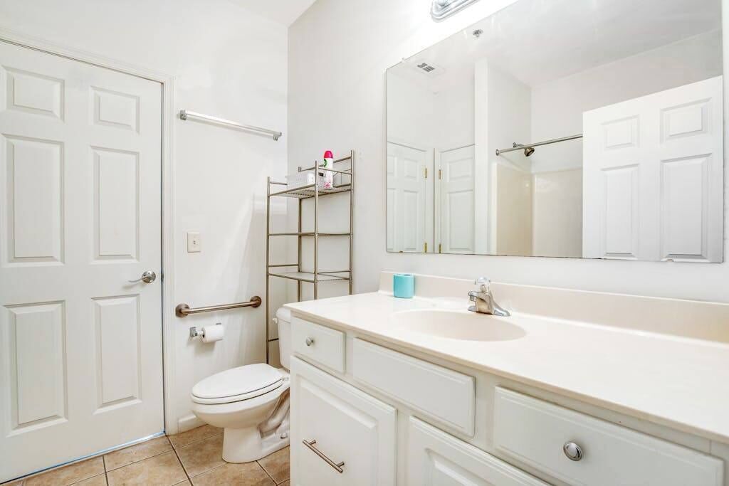Un bagno con un water bianco, un lavandino, uno specchio e uno scaffale metallico con articoli da toilette.