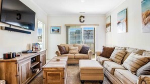 A living room with a sofa, ottoman, coffee table, TV, and a cabinet. - Sandpiper Villages condo with fast WiFi, private patio & more - near the beach (Rehoboth Beach)