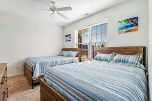 A bedroom with two beds, a ceiling fan, a window with blinds, and a painting on the wall.