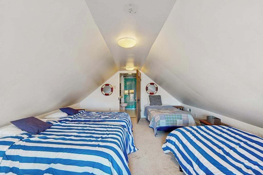 Ein quadratisches Schlafzimmer im Dachgeschoss mit zwei Betten, einer Tür zu einem Badezimmer und einer Deckenleuchte.