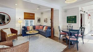 A modern living room with a sofa, coffee table, and dining area. A sign reads 'SLOW NO WAKE.' - Town of Lewes house w/deck, balcony, close to beach & restaurants (Lewes)