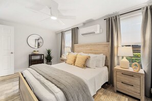 A modern bedroom with a bed, bedside tables, a mirror, an air conditioning unit, and a ceiling fan. - Dog-friendly Rehoboth Beach cottage steps from the beach & boardwalk with AC (Rehoboth Beach)