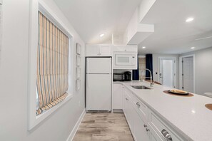 Eine moderne Küche mit weißen Schränken, einer eingebauten Mikrowelle, einem Kühlschrank und einem Spülbecken mit Armatur.