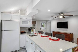 A modern kitchen with white cabinetry, a central island with red placemats, a microwave, and a ceiling fan. - Dog-friendly Rehoboth Beach cottage steps from the beach & boardwalk with AC (Rehoboth Beach)
