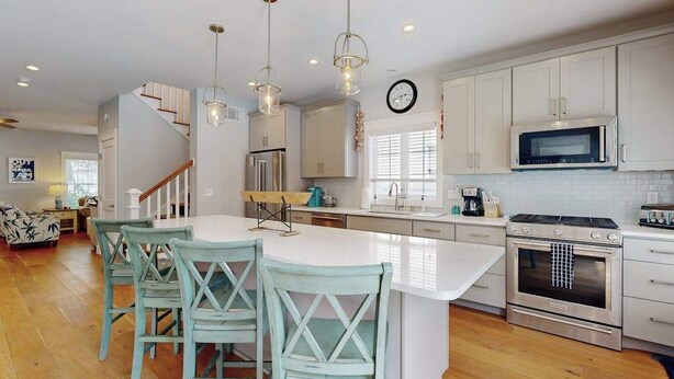 A modern kitchen with white cabinets, stainless steel appliances, a central island with bar stools, and pendant lighting. - Dog-friendly, 2-story home near beach with private outdoor pool, W/D & AC (Rehoboth Beach)