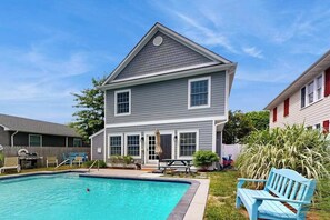 Ein zweistöckiges Haus mit Swimmingpool, einer Terrasse mit Stühlen und einem kleinen Garten.