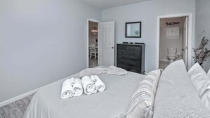 A bedroom with a bed, a dresser, a mirror, and a door leading to a bathroom. - Villas at Bay Crossing dog-friendly condo with pool, balcony, water views, & W/D (Lewes)