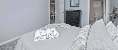 A bedroom with a bed, a dresser, a mirror, and a door leading to a bathroom.