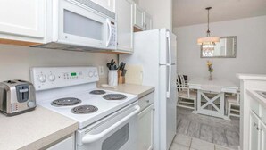 A compact kitchen with a stove, microwave, toaster, and refrigerator. - Villas at Bay Crossing dog-friendly condo with pool, balcony, water views, & W/D (Lewes)
