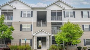 A multi-story building with a central entrance, balconies, and a parking lot. - Villas at Bay Crossing dog-friendly condo with pool, balcony, water views, & W/D (Lewes)