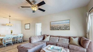 A living room with a sectional sofa, a ceiling fan, a dining table with chairs, and a painting on the wall. - Villas at Bay Crossing dog-friendly condo with pool, balcony, water views, & W/D (Lewes)