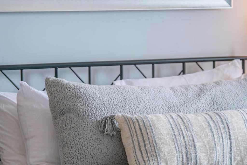Un lit avec un cadre en métal, des oreillers blancs et un oreiller gris à texture.