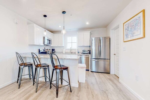 A modern kitchen with white cabinets, stainless steel appliances, and a bar area with stools. - Rehoboth Beach House with amazing pool, washer/dryer, & clubhouse (Rehoboth Beach)