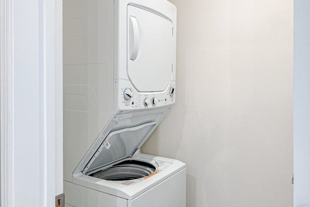 A compact, wall-mounted washer and dryer unit in a bathroom with a plain wall background.