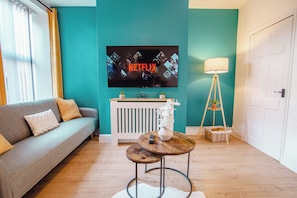 A living room with a sofa, a TV mounted on the wall, a lamp, and a small table with a vase and remote control. - Modern Escape Oasis | Free Parking | 14PPL (Sheffield)
