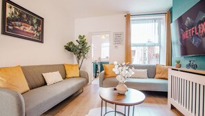 Ein Wohnzimmer mit zwei Sofas, einem Couchtisch, einem gerahmten Bild und einem Fernseher, der 'NETFLIX' anzeigt.