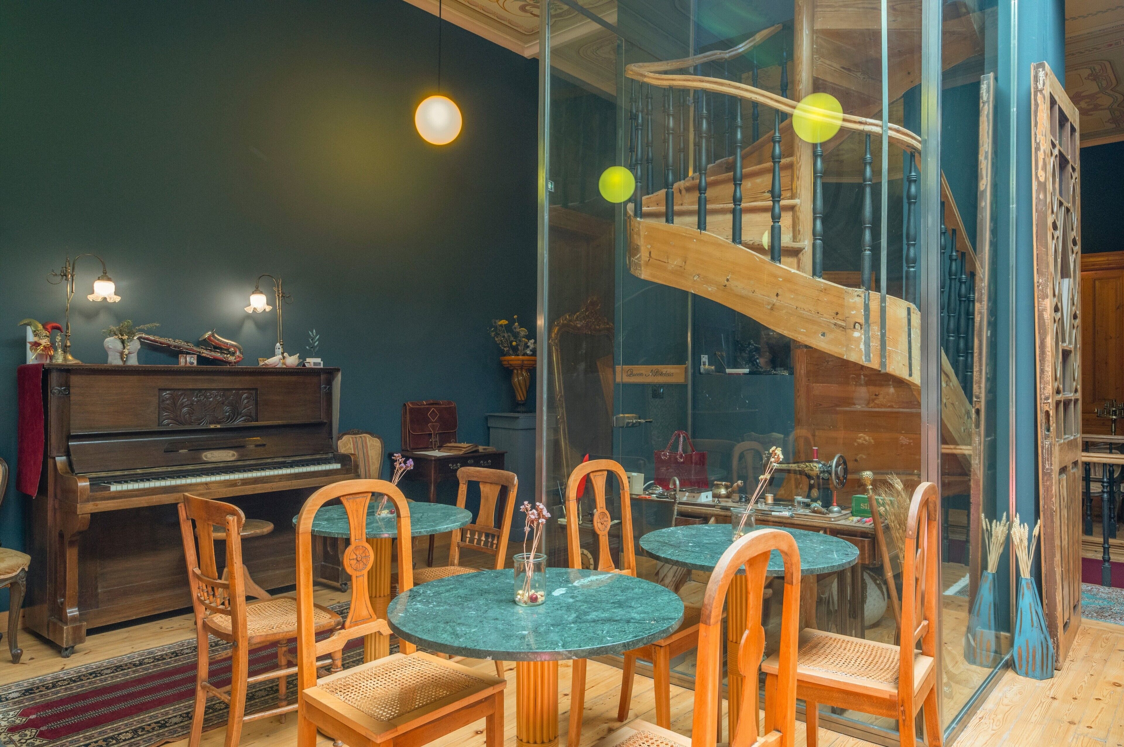 Una habitación con un piano, sillas de madera, una mesa de cristal y una escalera en espiral.