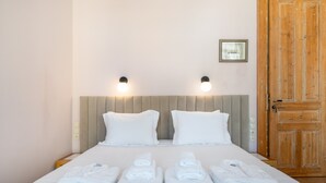 Ein ordentlich bezogenes Bett mit weißen Leinen und Handtüchern, zwei an der Wand befestigte Lampen und eine Holztür.