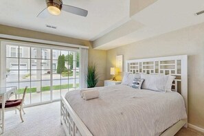 A bedroom with a large bed, a ceiling fan, a window with a view of the outside, and a nightstand with a lamp. - 3-story townhouse close to beach & shops w/screened porch, on-site pool & gym (Rehoboth Beach)