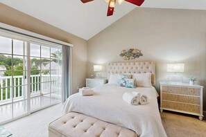 A bedroom with a large window, a bed with a tufted headboard, bedside tables with lamps, and a decorative wall piece. - 3-story townhouse close to beach & shops w/screened porch, on-site pool & gym (Rehoboth Beach)