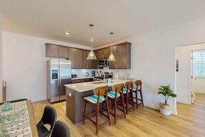 Una cocina moderna con una isla central, taburetes de bar, electrodomésticos de acero inoxidable, iluminación colgante y una planta en maceta.