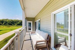 A covered porch with a sliding glass door, a white outdoor bench, and a view of a green landscape. - The Residences at Rehoboth Bay condo w/community pool and patio (Lewes)