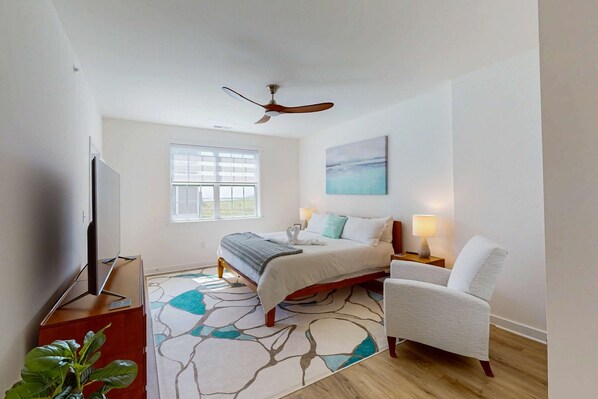A bedroom with a bed, a chair, a TV, a ceiling fan, a window, and a painting. - The Residences at Rehoboth Bay condo w/community pool and patio (Lewes)
