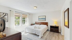 Ein Schlafzimmer mit Bett, Nachttischen, einer Lampe, einem Bild und einem Fenster mit Vorhängen.