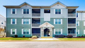 A multi-story residential building with a central entrance, balconies, and a flat roof. - Sandpiper Village dog-friendly condo with patio, AC & close access to everything (Rehoboth Beach)