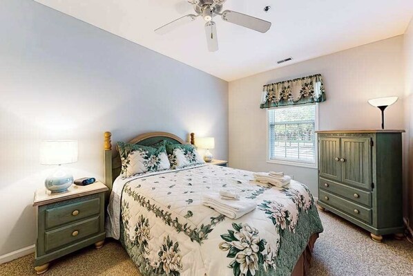 A bedroom with a bed, nightstands, a wardrobe, a ceiling fan, and a window with curtains. - Sandpiper Village dog-friendly condo with patio, AC & close access to everything (Rehoboth Beach)
