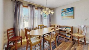Een eetgedeelte met een houten tafel en stoelen, een kroonluchter, een boekenkast en een schilderij aan de muur.