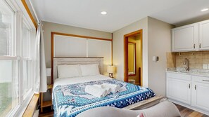 A hotel room with a bed, a nightstand, a lamp, a bathroom with a sink, and a view of the outdoors. - Dog-Friendly Rehoboth Beach Retreat w/ central AC, Updated Kitchen & Fire Pit (Rehoboth Beach)