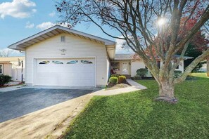 Ein eingeschossiges Haus mit Garage, ein kleiner Vorgarten mit Baum und ein klarer Himmel.