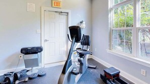 Ein Fitnessraum mit Trainingsgeräten, einer Tür und einem Fenster mit Blick auf Bäume.
