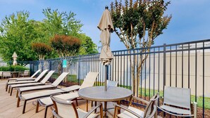 Eine Terrasse mit runden Tischen und Stühlen, einem überdachten Sonnenschirm und einem Metallzaun.