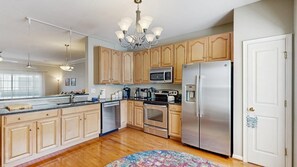 A modern kitchen with wooden cabinets, stainless steel appliances, and a chandelier. - Rehoboth Crossing townhouse with pool, gym, balcony, grill, W/D, bikes, & patio (Rehoboth Beach)