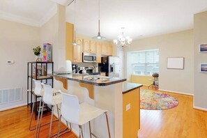 A modern kitchen with a central island, bar stools, and a chandelier. - Rehoboth Crossing townhouse with pool, gym, balcony, grill, W/D, bikes, & patio (Rehoboth Beach)