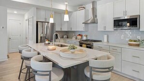 Una cocina moderna con armarios blancos, electrodomésticos de acero inoxidable y una isla central con taburetes de bar.